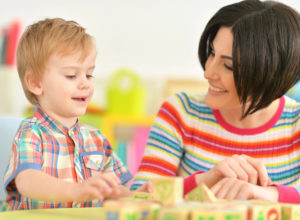 Seated at a table with blocks, grownup is smiling at a youn child